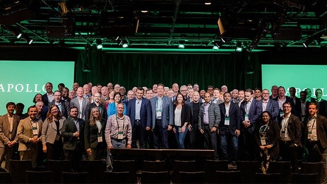 Large group of people in business attire standing on a stage in front of green screens displaying “APOLLO”—depicting a corporate event focused on private equity for digital and technology industries 