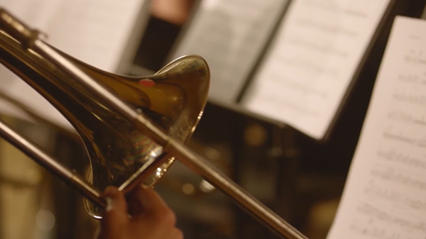 Close-up of a brass trombone. Music sheets appear blurred in the background, illustrating a case study about asset-backed finance deals with music company, concord.  